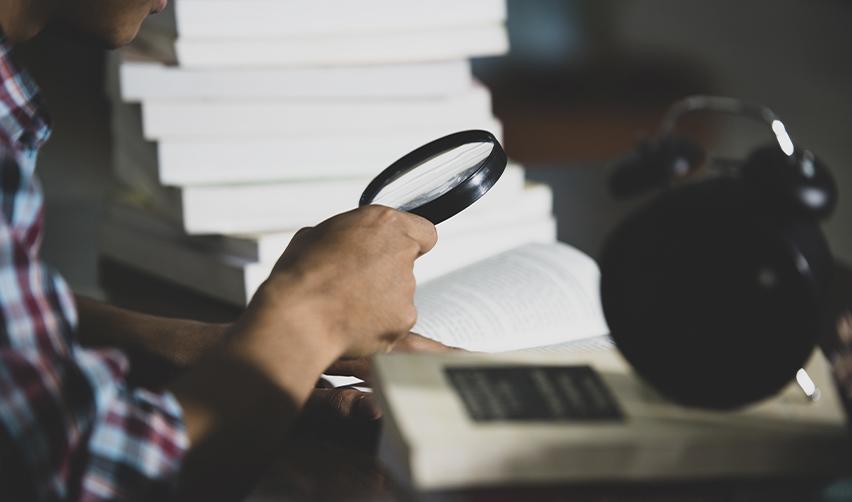 Close-up of a person using a magnifying glass to examine documents, representing the importance of accuracy and consistency in EB5 visa petition documentation.
