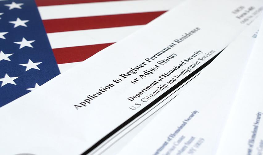 An adjustment of status form with the US flag in the background, representing the EB5 visa process for obtaining a Green Card.