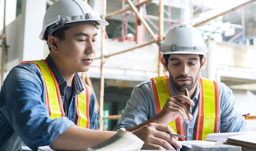 Two engineers in hard hats reviewing plans, representing employment-based non-immigrant visas like H1B and L1 in the US.