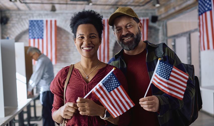 Couple smiling and holding American flags in a citizenship ceremony, symbolizing the benefits of immigrant visas and Green Card pathways.