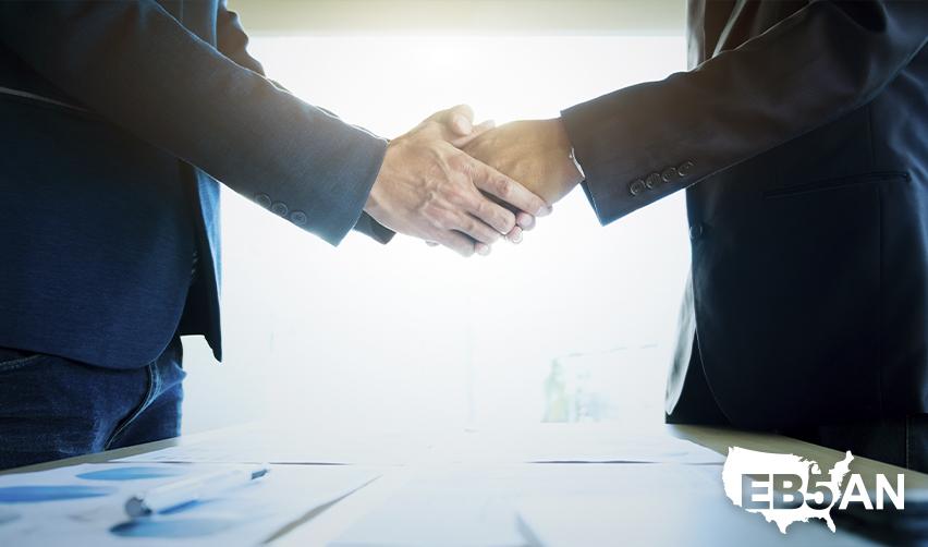 Two professionals shaking hands over a desk, representing collaboration for obtaining employment-based green cards with the guidance of an immigration attorney.