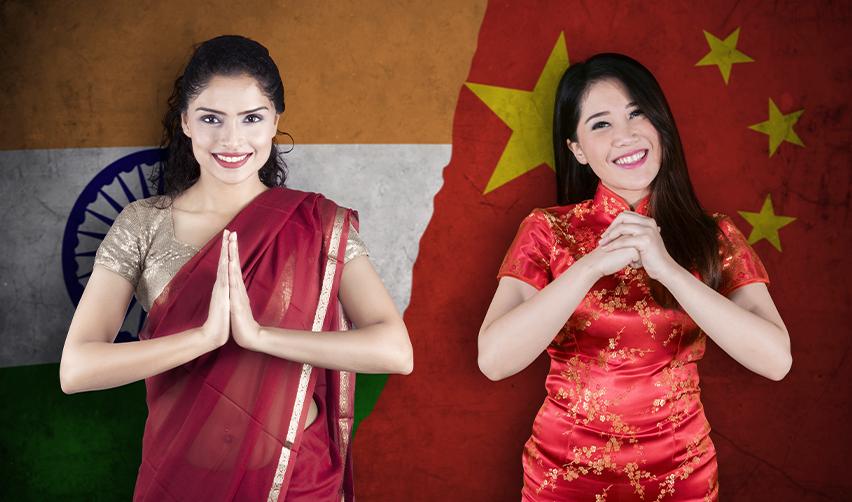 A woman in traditional Indian attire and another woman in a red Chinese qipao pose with smiles against a backdrop of the Indian and Chinese flags. This visual represents EB5 visa opportunities for investors from India and China.