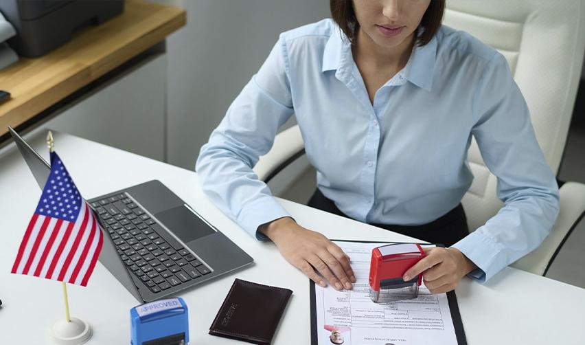 Immigration officer stamping a decision on a visa application with the U.S. flag on the desk, symbolizing EB5 visa backlogs.