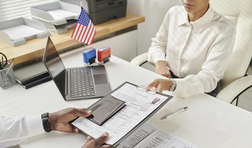 Immigration official reviewing EB5 application documents with an applicant in an office with an American flag in the background, symbolizing consular processing.