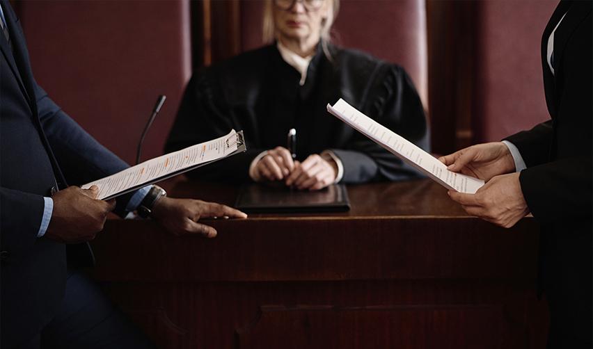 Two immigration attorneys presenting legal documents in a courtroom with a judge presiding in the background, representing the Battineni case and its significance for EB5 source of funds and path of funds requirements.