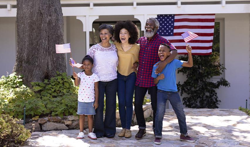 A multigenerational family joyfully celebrating in front of an American flag, symbolizing the benefits of obtaining U.S. permanent residency through the EB5 program.
