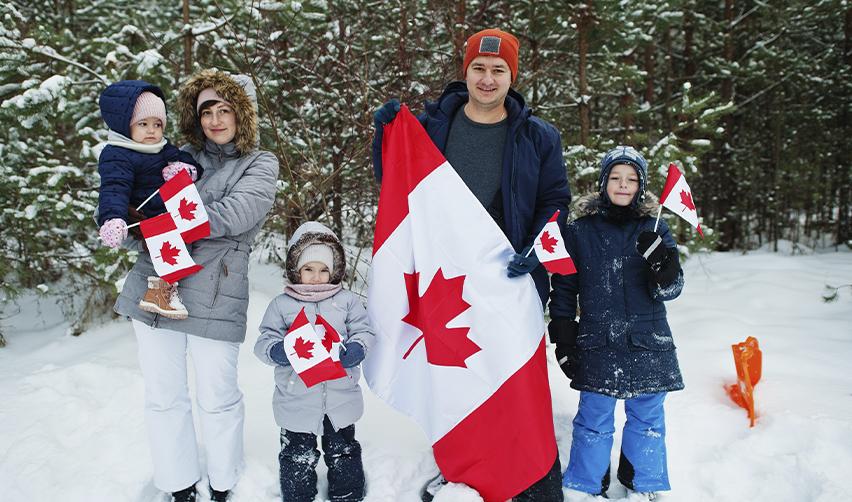A family of five standing in a snowy forest, holding Canadian flags. Highlights the journey of Canadian families considering U.S. green card opportunities, including EB5 investments.