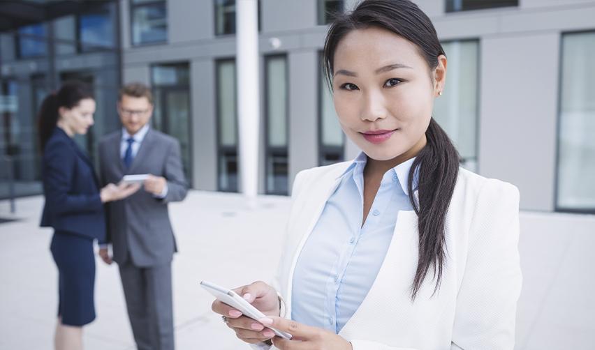 A confident Asian businesswoman holding a smartphone with a professional setting in the background, representing the benefits of reserved EB5 visas for investors from China and other countries.