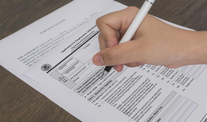 Hand signing an employment authorization document application form, representing the process for EB5 investors to work legally in the U.S.