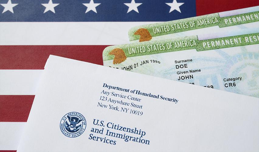 U.S. Green Cards and Department of Homeland Security - USCIS document on top of an American flag, symbolizing permanent residency benefits of the EB5 program.
