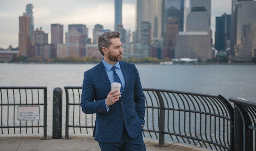 A Canadian citizen in a suit standing by a waterfront with a city skyline in the background. Illustrates the success of Canadian investors and entrepreneurs leveraging the EB5 immigration process for U.S. green card acquisition.