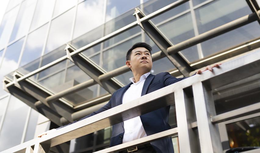Confident businessman in a suit standing outside a modern office building, looking ahead. The security and long-term benefits of the EB5 visa as a direct path to U.S. residency.