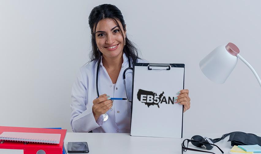 A smiling doctor holding a clipboard with the EB5AN logo, representing how the EB5 visa program helps Indian doctors achieve green card residency faster.