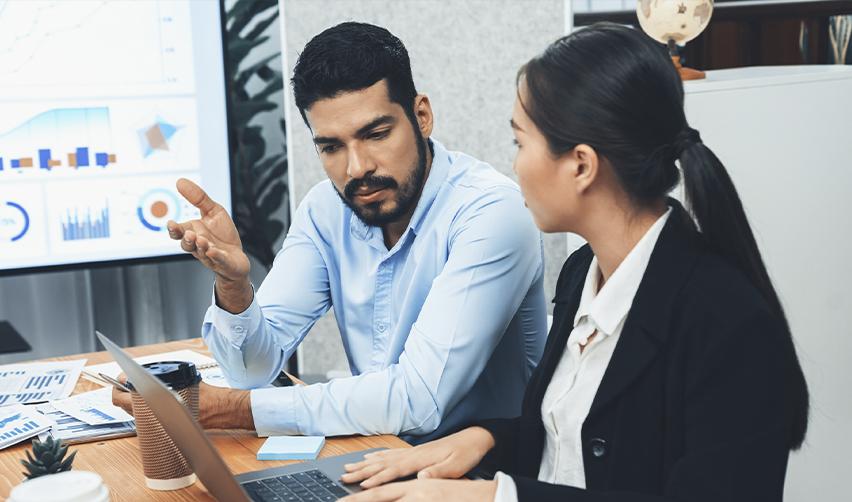 Two professionals discussing visa backlog concerns and EB5 investment options with data charts on a screen in the background.