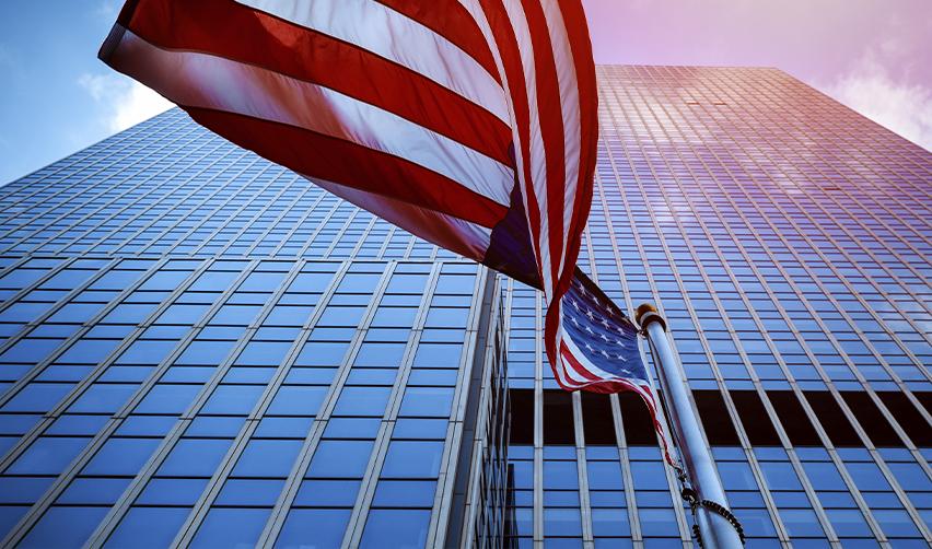 Low-angle view of an American flag waving in front of modern skyscrapers, symbolizing investment opportunities in the U.S. through the EB5 program.