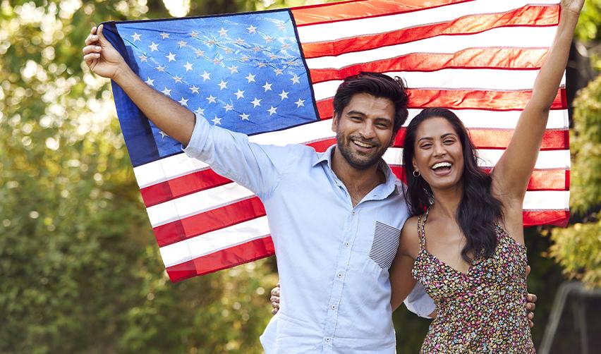 Happy Indian couple holding an American flag, symbolizing the success of obtaining a Green Card through EB5 rural TEA investments.