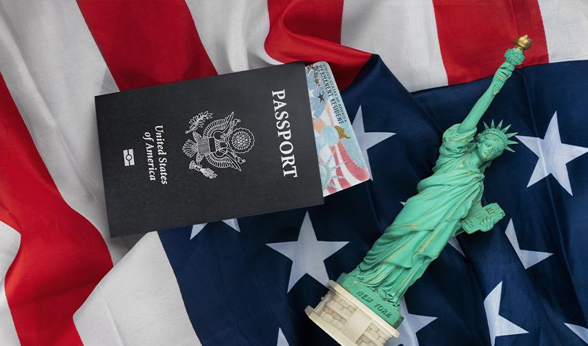 United States passport placed on an American flag with a small Statue of Liberty replica. The EB5 visa as a direct path to a Green Card and U.S. citizenship for EB5AN investors.