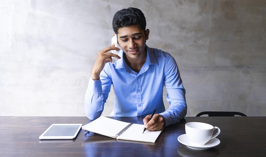 Indian entrepreneur making notes while on a call, discussing EB5 visa benefits and filing strategies.