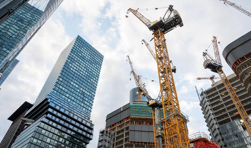 A city skyline with multiple high-rise buildings under construction, surrounded by yellow cranes. EB5 investment capital plays a key role in funding real estate developments, revitalizing urban areas, and generating jobs.