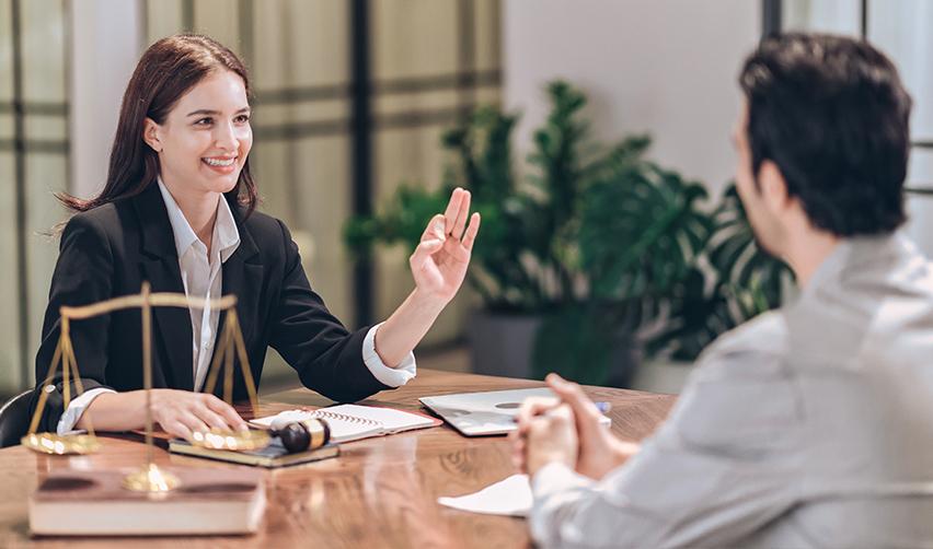 An EB5 attorney smiling while speaking with a client, with legal scales, a gavel, and documents on the desk. Depicts a helpful EB5 lawyer providing guidance to an EB5 investor.