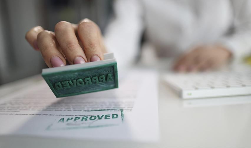 Close-up of an immigration official stamping “APPROVED” on a document, symbolizing high EB5 approval rates and faster petition processing for eb5 rural TEA investors.