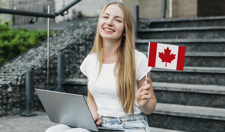 A cheerful Canadian citizen holding a Canadian flag while working on a laptop, highlighting opportunities for skilled workers and students to immigrate to the U.S. through various visas like the EB5 visa or the TN visa.