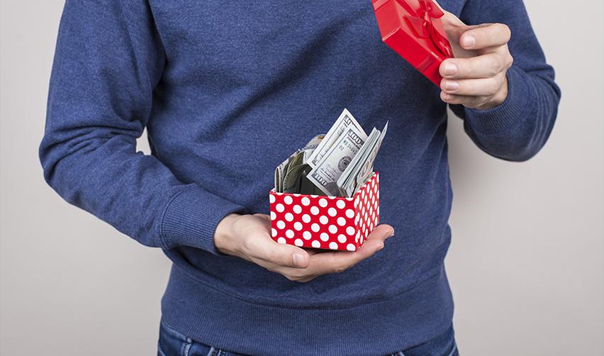 A person holding a red gift box filled with U.S. dollar bills, symbolizing how F1 students can use cash gifts from parents or relatives to finance their EB5 investment for a Green Card.