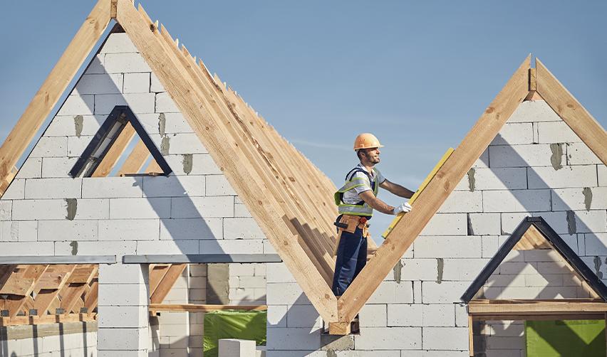A construction worker measuring the wooden roof frame of a newly built house, highlighting the role of EB5 capital in funding single-family home developments and real estate projects under the EB5 Immigrant Investor Program.
