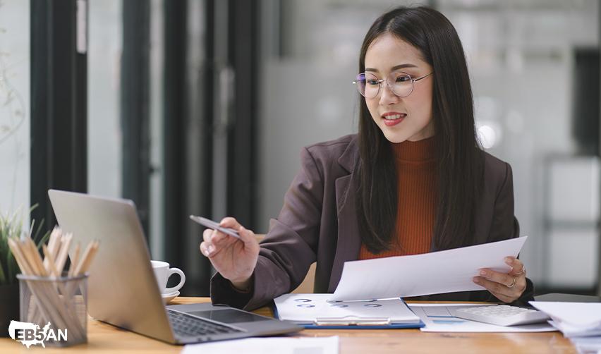 The EB5AN logo next to an EB5 investor reviewing tax documents at her laptop. Learn about K1 forms, taxable income, and U.S. tax filing requirements for EB5 investments.