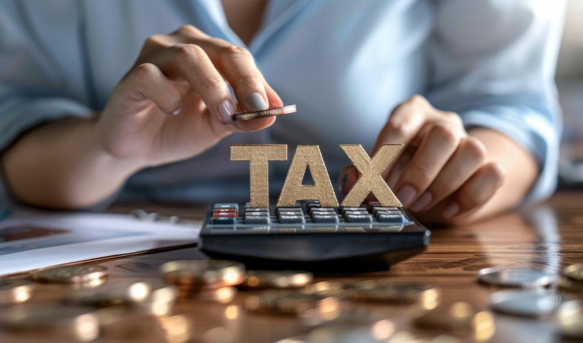 A person stacks coins on a calculator labeled 'TAX.' Understanding EB5 investment taxation and preferred returns.