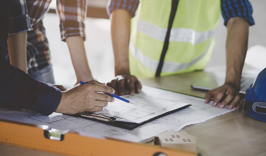 A group of professionals examines construction plans, highlighting the role of skilled immigrant workers, like H1B visa holders, in industries affected by stricter visa requirements and temporary protected status policies.