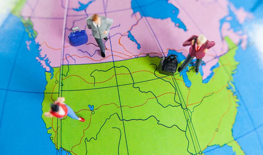 Miniature travelers standing on a North America map with suitcases, symbolizing Canadian migration to the U.S. through the EB5 Green Card.