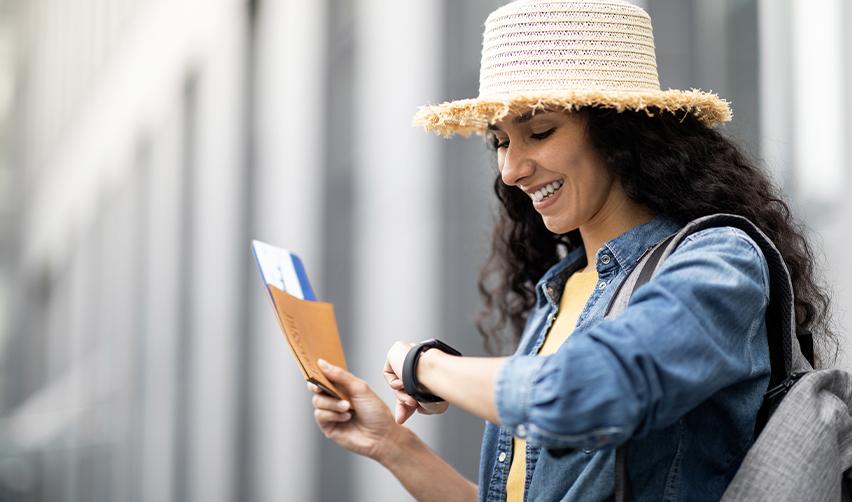Female EB5 applicant checking time before boarding international flight, holding passport and travel documents.