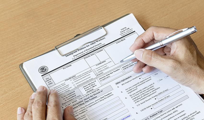 Close-up of a person filling out Form I-140 for a Green Card petition, illustrating the importance of ensuring immigration paperwork is timely filed with the United States Citizenship and Immigration Services.