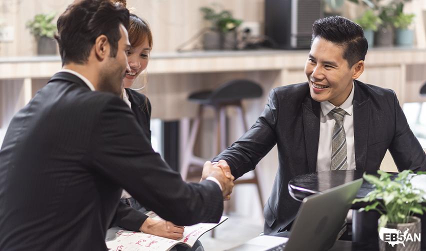 The EB5AN logo next to Foreign investors sealing a business deal in a casual setting, representing the EB5 program’s pathway to conditional permanent resident status through targeted employment area investment.