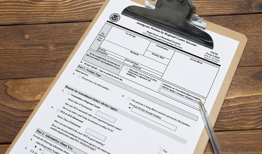 USCIS I-526E form on a clipboard, representing EB5 visa application process for foreign nationals, emphasizing compliance with immigration law.