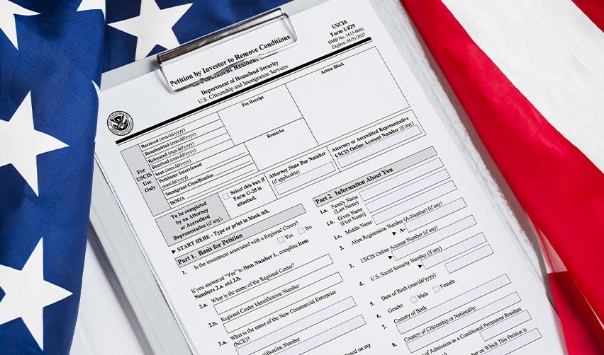 Form I-829 on a clipboard with an American flag, illustrating the process of removing conditions on an EB5 Green Card.