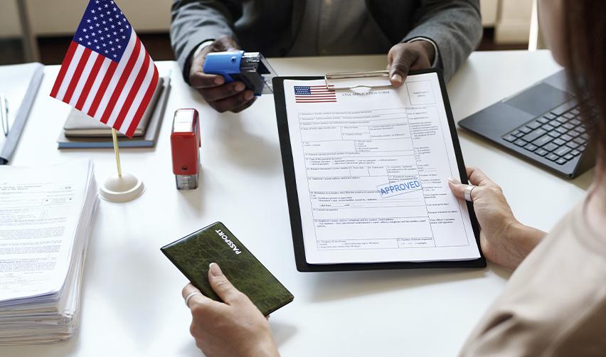 Immigration officer approving a visa application at a desk with U.S. flag and passport, illustrating successful EB5 visa processing and approval through adjustment of status or consular processing.