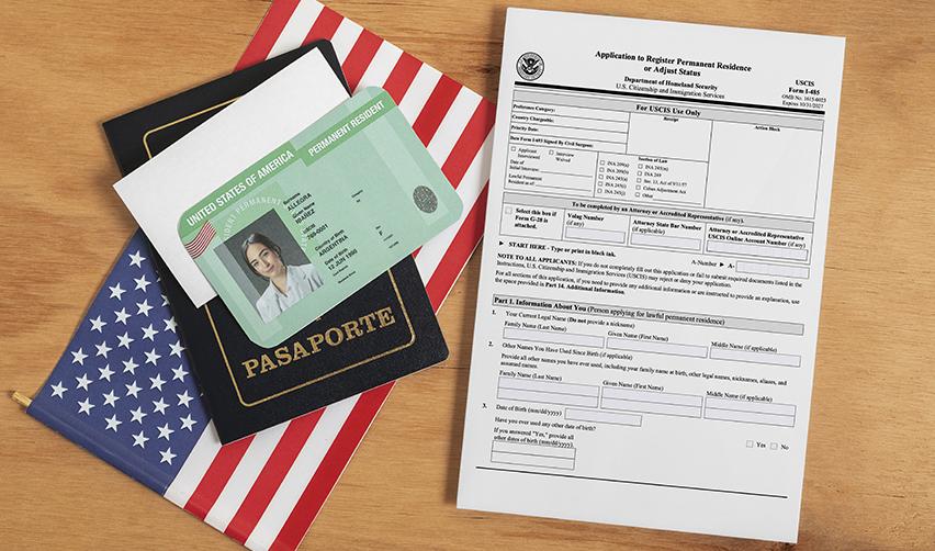 U.S. passport, Green Card, and Form I-485 on a wooden table with the American flag, representing the EB5 adjustment of status process.