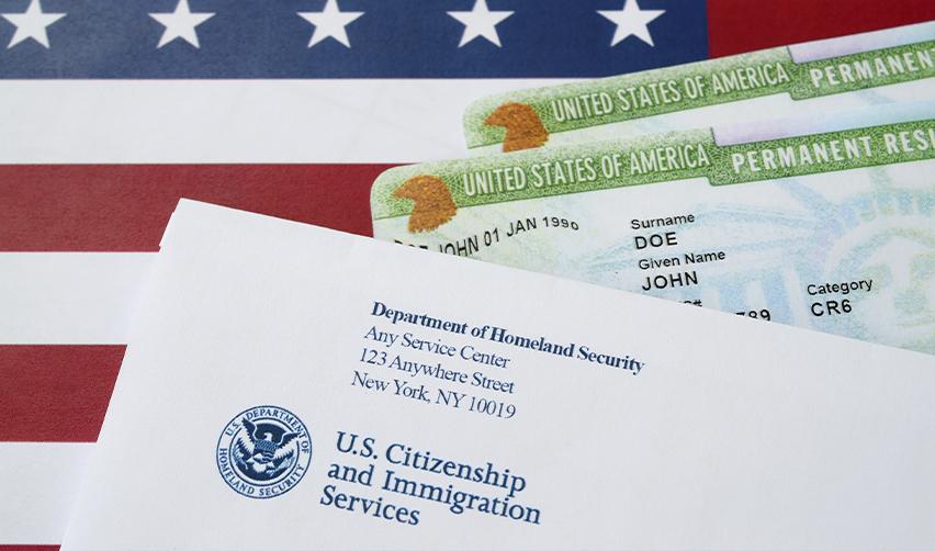 U.S. Green Cards and a USCIS envelope on top of an American flag, representing the differences between a green card vs citizenship.