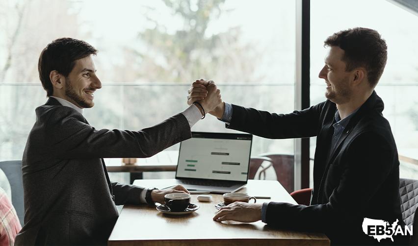 Two professionals shaking hands over a laptop, representing partnership with an EB5 team like EB5AN for investment documentation and compliance.
