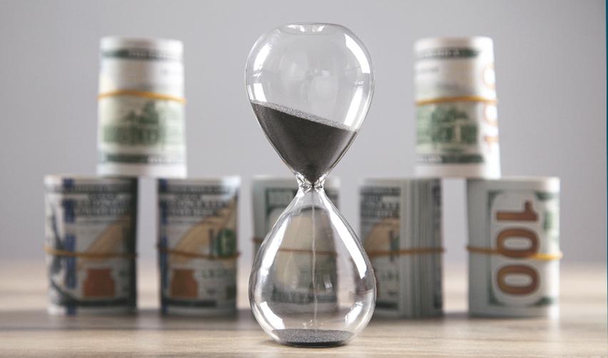 Hourglass with sand running next to stacks of U.S. dollars, illustrating the critical timing aspect of EB5 visa investments and potential cost of delays.