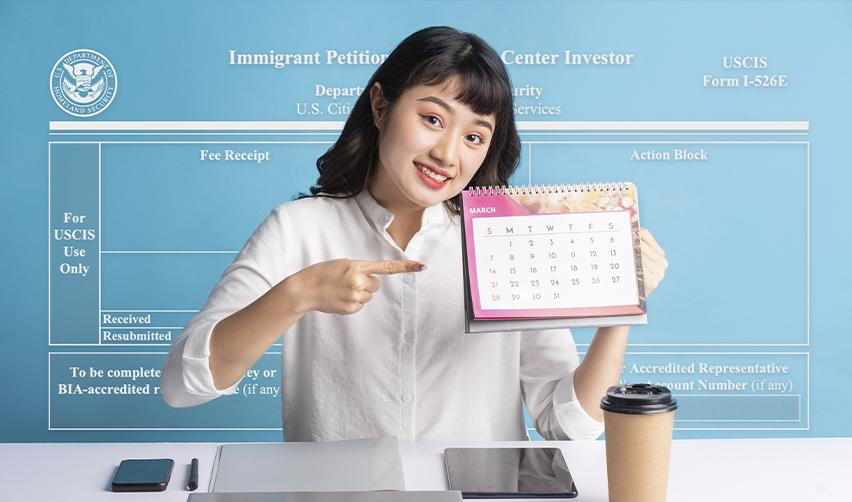 Smiling woman pointing to a calendar date in front of a Form I-526E backdrop, highlighting how EB5 timelines are tied to each fiscal year.