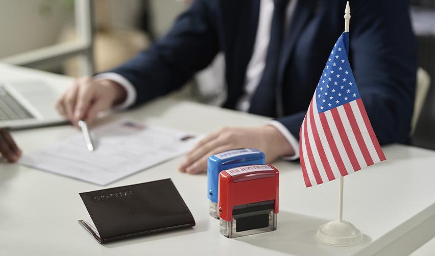 U.S. immigration officer reviews EB5 petition documents with approval and rejection stamps and a U.S. flag on the desk.