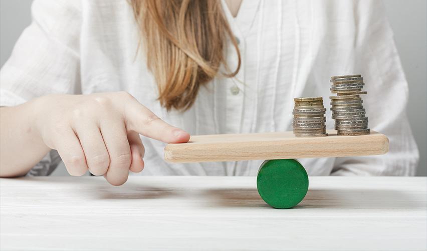 Coins balanced on a wooden seesaw, illustrating the lower capital requirement and risk-reward considerations of EB5 TEA investments.
