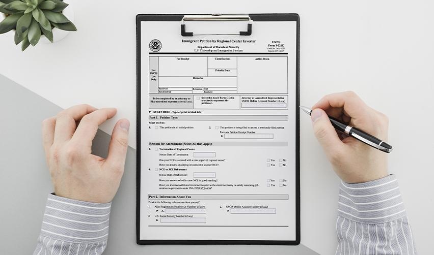 A person filling out the USCIS Form I-526E on a clipboard, representing the EB5 investor petition process and importance of compliance before fund release.