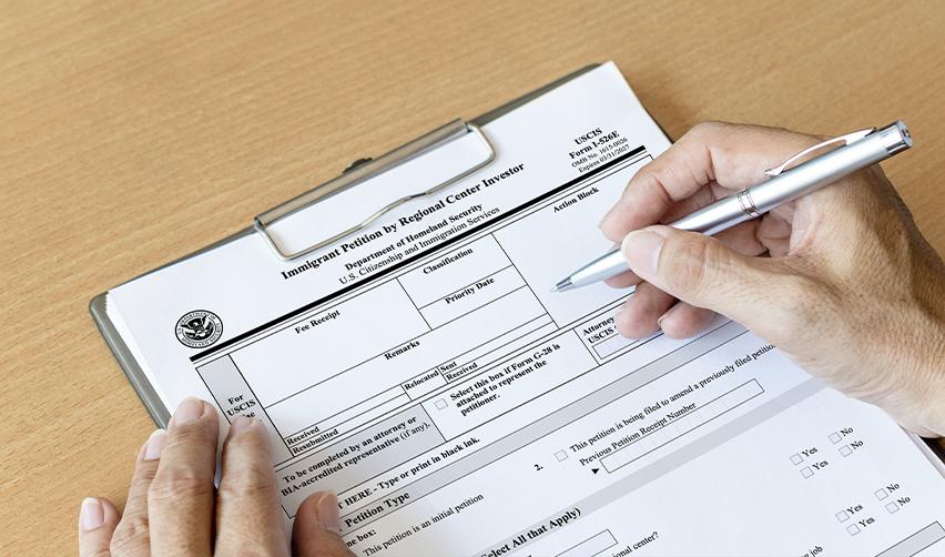 Close-up of hands filling out USCIS Form I-526E, the EB5 immigrant petition by a regional center investor.