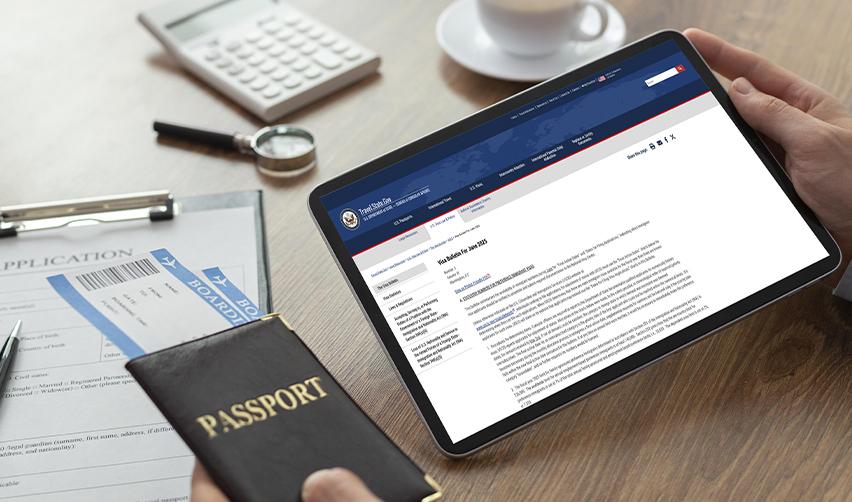 Foreign investors reviewing the monthly Visa Bulletin on a tablet next to a passport and boarding pass, assessing the availability of immigrant visas this fiscal year.