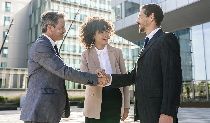 Business partners smiling and shaking hands outside a modern office building, symbolizing trust and strong communication between EB5 investors and regional centers.
