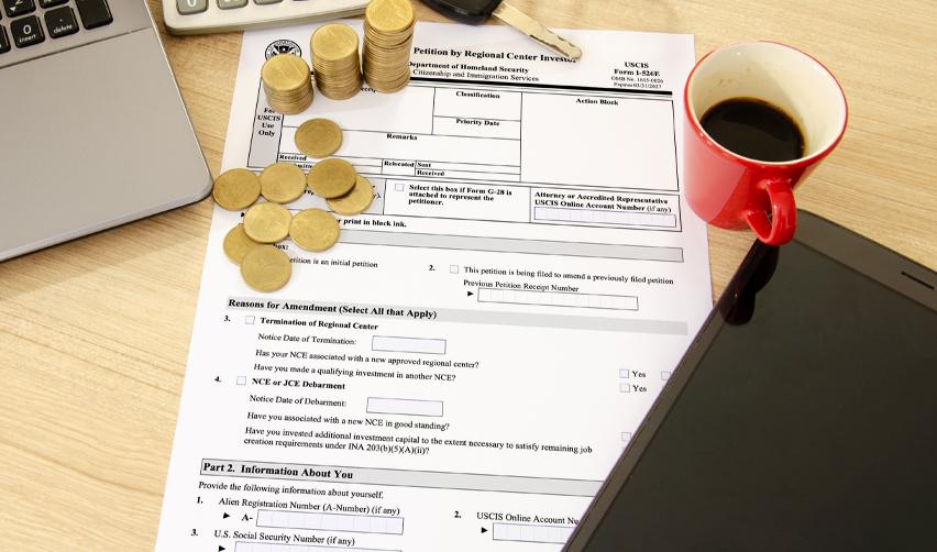 A stack of coins and a coffee mug on top of a USCIS petition form, representing the role of regional centers in the EB5 process.